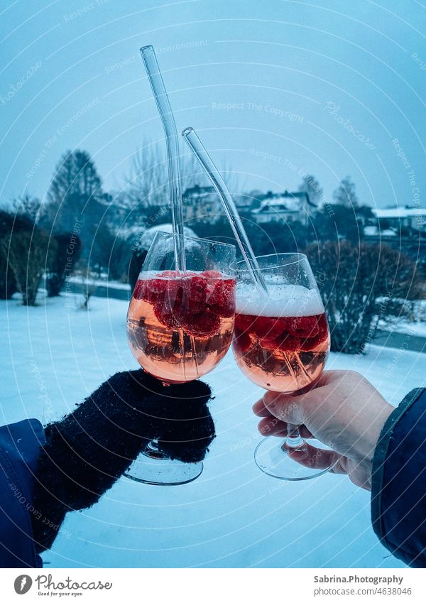 Two hands toasting with cold. alcoholic drink with raspberries and glass straw in snow - Bromskirchen, North Rhine-Westphalia, Germany Winter Snow toast drinks
