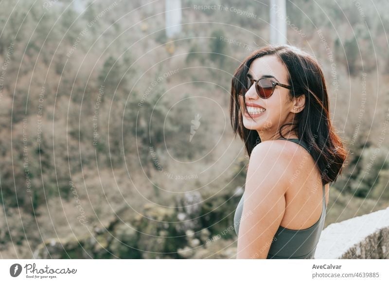 A young woman traveler in sporty clothes and sunglasses with looking from a cliff in the forest, admiring the views of the wildlife. Healthy life at the nature young people concept.