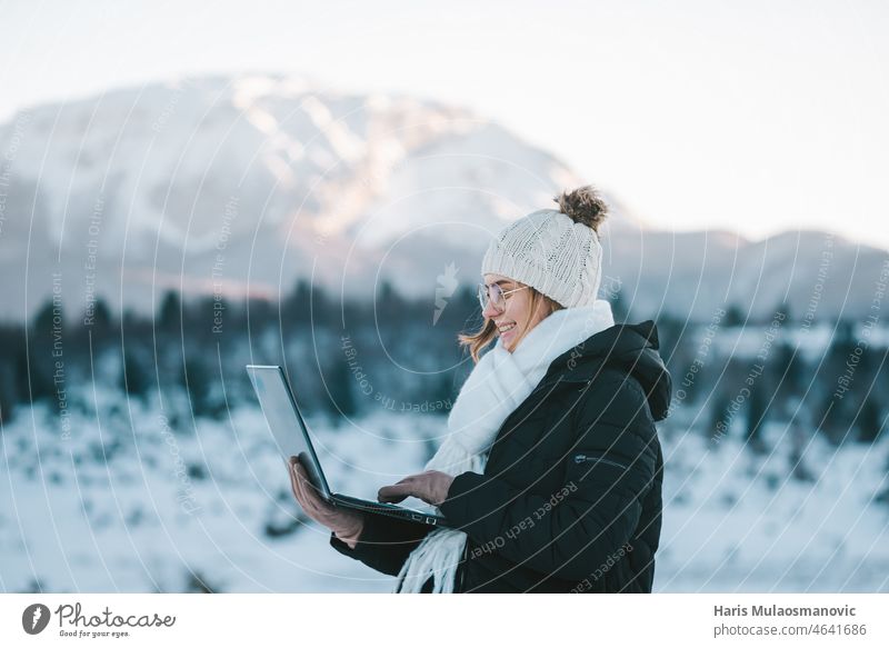 young smiling woman freelancer using laptop outdoors in snow mountains 5g adventure beautiful cold communication digital nomad forest freedom fun girl happy