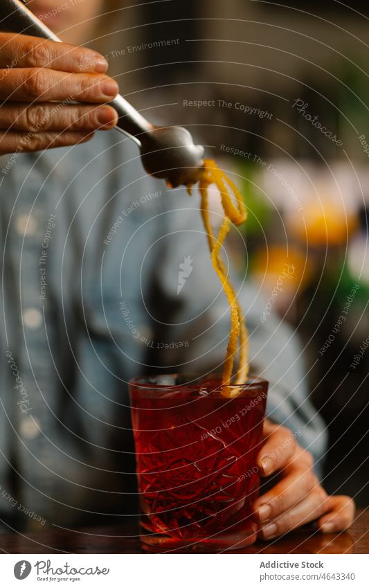 Anonymous bartender adding lemon zest in cocktail old fashioned beverage alcohol serve booze work counter glass concentrate pub drink cafe fruit sour decorate