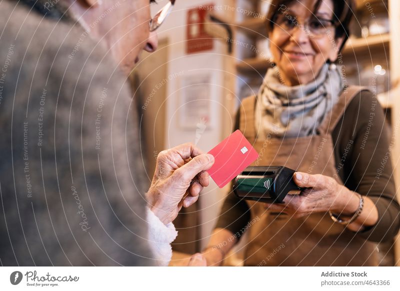 Anonymous elderly woman using credit card while doing payment in eco shop women customer terminal positive senior seller store female commerce eco friendly