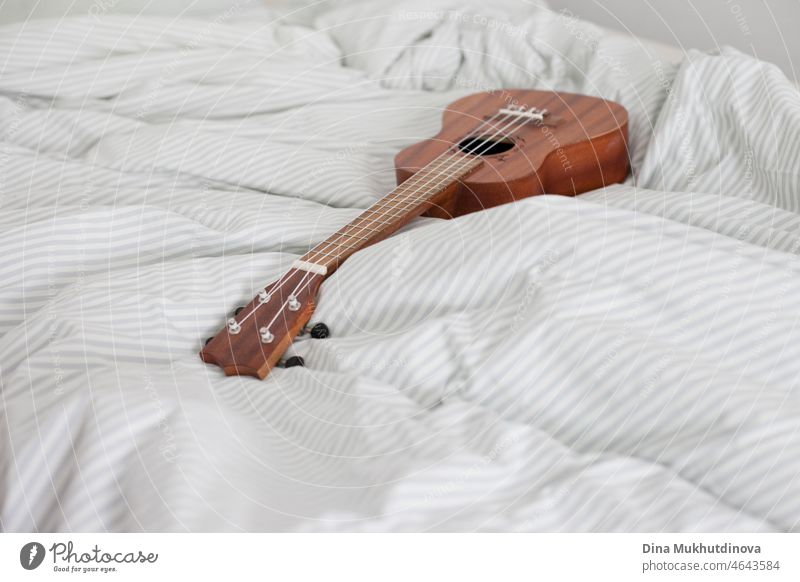 Ukulele guiutar lying on the bed on the white striped blanket. Hobby and playing music at cozy home. Minimalism scandinavian style home. bedroom indoor melody