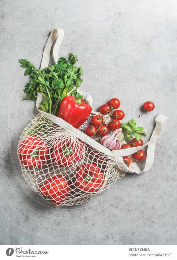 Various vegetables and herbs in reusable plastic free shopping bag various grey concrete kitchen red bell pepper tomatoes cilantro garlic sustainable lifestyle