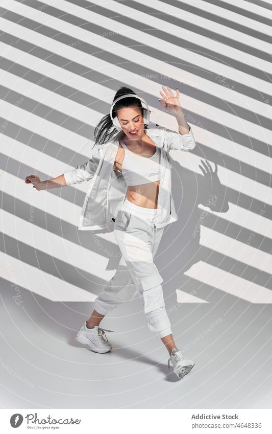 Young woman dancing hip hop in striped studio dancer freestyle headphones hobby shadow perform listen happy rehearsal music female skill song gadget slim
