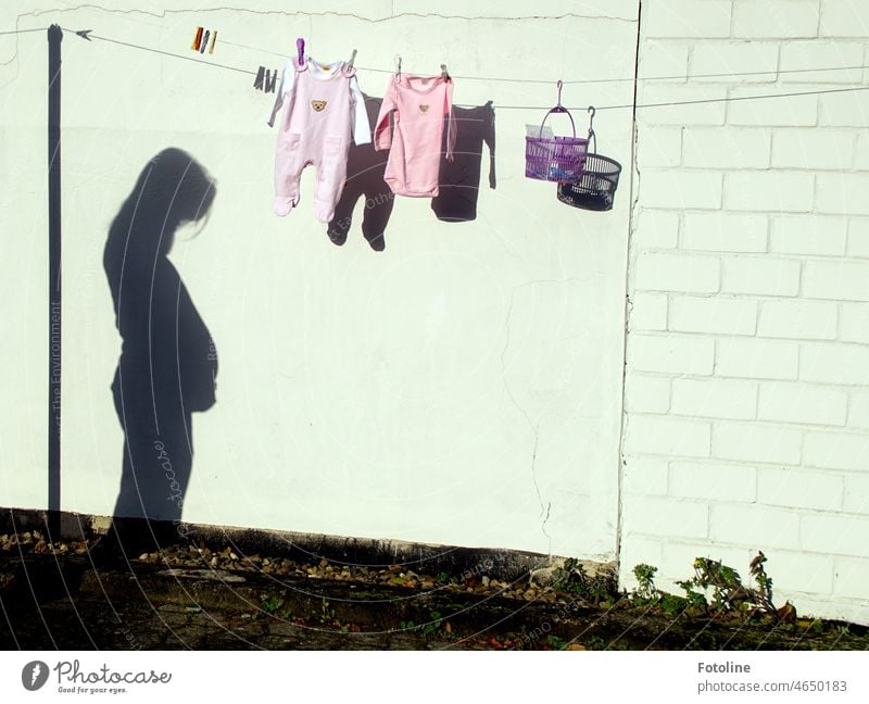 In joyful expectation - On a clothesline hangs freshly washed baby clothes  and a basket with clips. The shadow of the expectant mother shows. it  won't be long before the baby comes. 