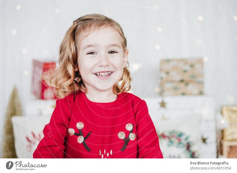 portrait of happy little girl wearing red christmas dress at home over christmas decoration. Holiday concept kid smiling caucasian blonde 3 year old toddler