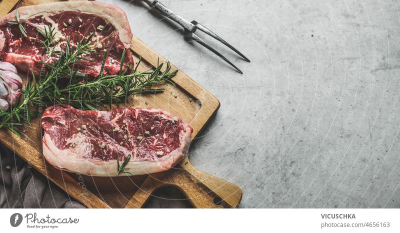 Raw beef steaks background with rosemary and green pepper raw wooden cutting board butcher fork close up preparing fresh meat top view copy space barbecue bbq