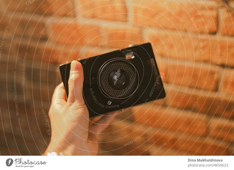 Hand holding retro vintage camera at a room with cozy lighting and red brick wall. Retro vintage photo camera in hand horizontal photo. retro camera film camera