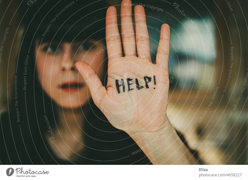 Young woman defensively holds a hand in front of her face on which the word Help is written Woman Protective ask for help Helpless Seeking help