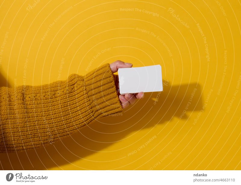 Female hand holding empty paper white business card on a yellow background. Copy space ad adult advertise advertisement arm blank caucasian communication female