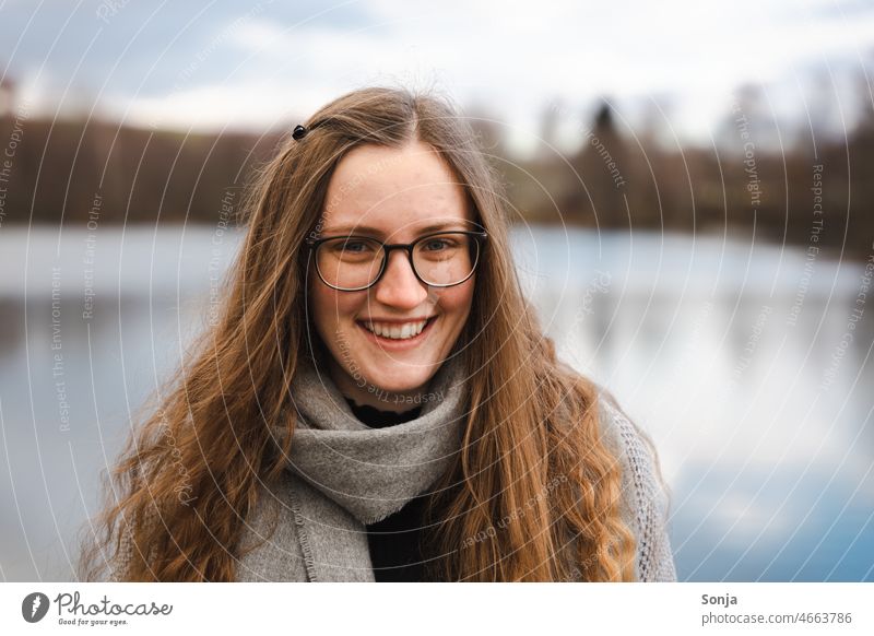 A young smiling woman with glasses and long hair by a lake. Young woman Smiling Feminine portrait long hairs pretty Attractive Exterior shot Happy Lifestyle