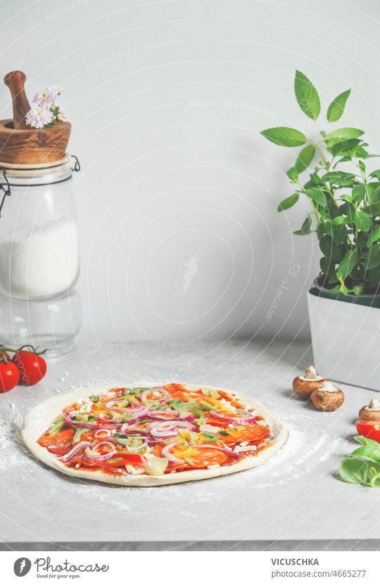 Homemade pizza at white kitchen table with glass jar with flour, basil and ingredients homemade cooking traditional italian food front view modern still life