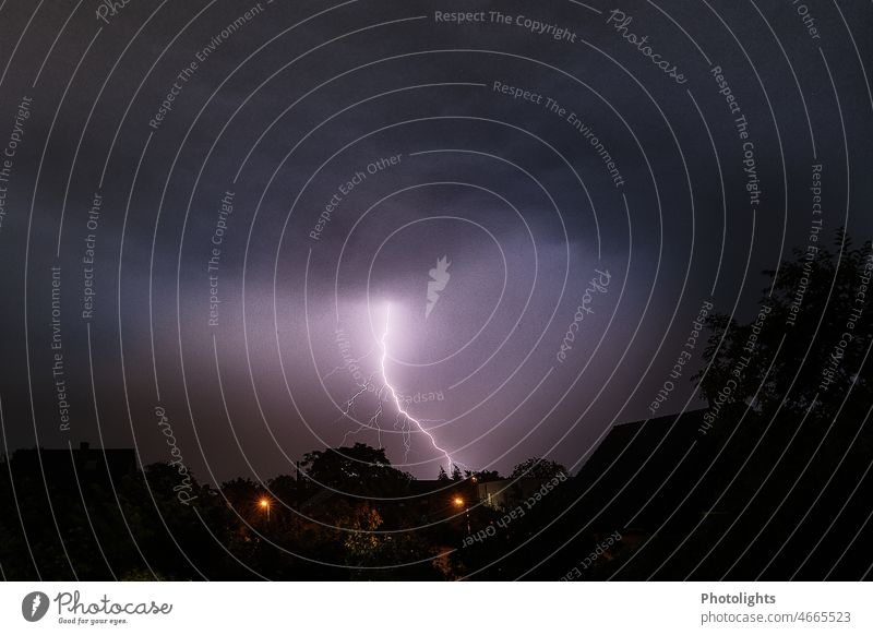 Thunderstorm II ! Lightning in the night sky. In the foreground house roofs and street lamps can be seen. Thunder and lightning Storm clouds Night