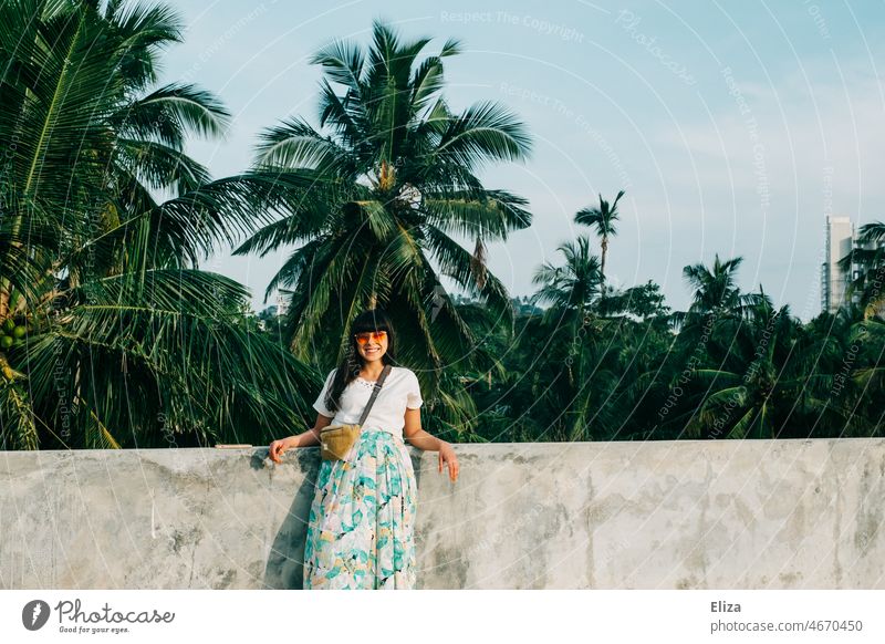Smiling woman with sunglasses leaning against a wall in front of palm trees. Good mood on vacation. palms Woman smilingly Summer Happiness tropics Vacation mood