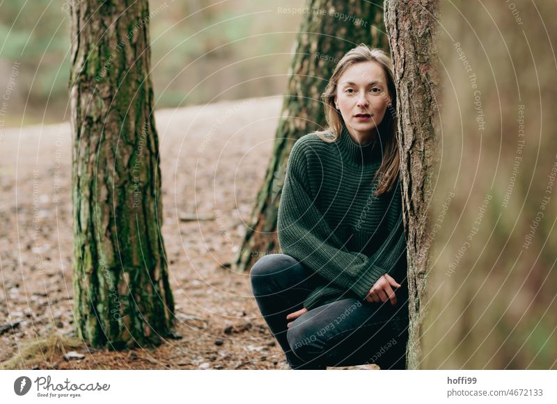 a woman behind trees looks tensely into the camera Looking Young woman melancholically portrait Tense Pensive Calm Meditative Forest Strand of hair Nature