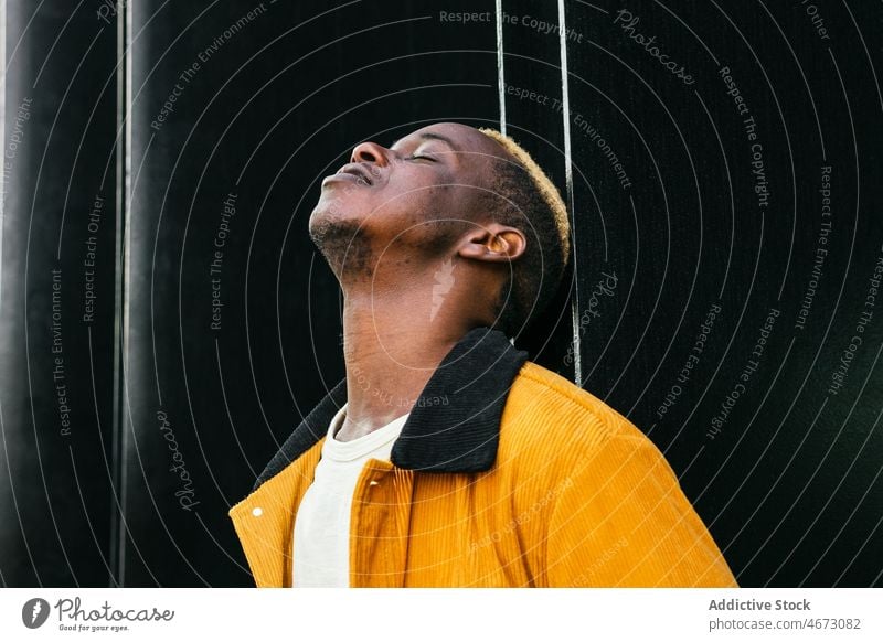 Cool young black man near building style trendy urban street style appearance fashion city dyed hair modern casual short hair wall dreamy pensive confident