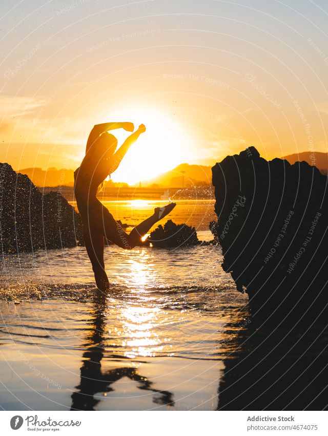 Anonymous man splashing water in sea at sunset time - a Royalty