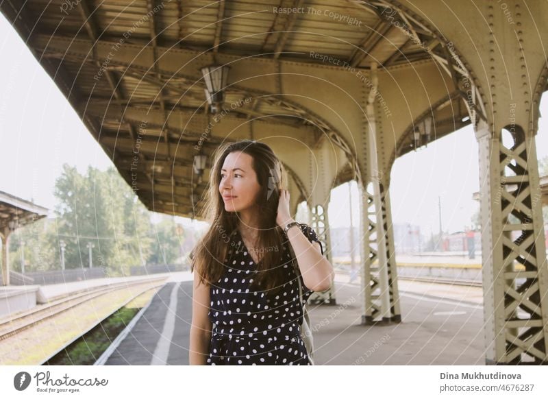 Young stylish millennial woman walking at an old railway station waiting for train. Beautiful woman tourist in casual dress in the city traveling.