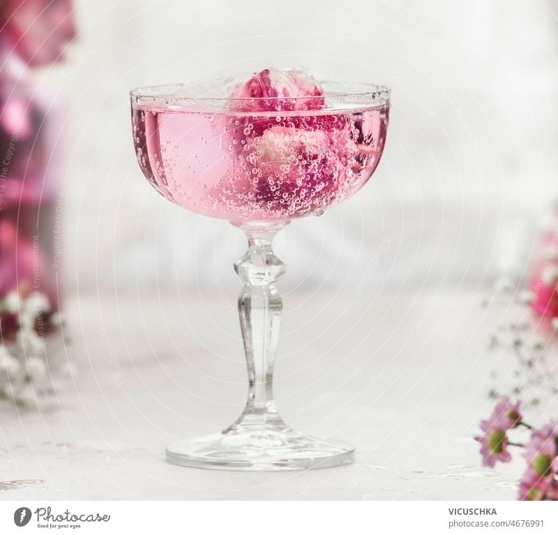 Close up of sparkling pink drink with rose petals in champagne glass close up white table blurred background aperitif elegant decoration celebration front view