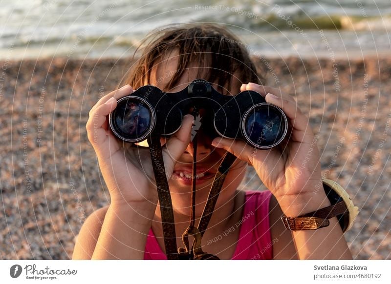 Tanned toddler girl with brown hair on the beach in summer looking through binoculars sunset child cute happy holiday kid sea smile travel vacation young