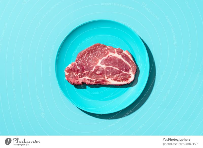 Raw pork steak on a plate, top view. Steak isolated on blue background above barbeque bbq beef bone bright butcher chop close-up color cuisine cut cutlet cyan