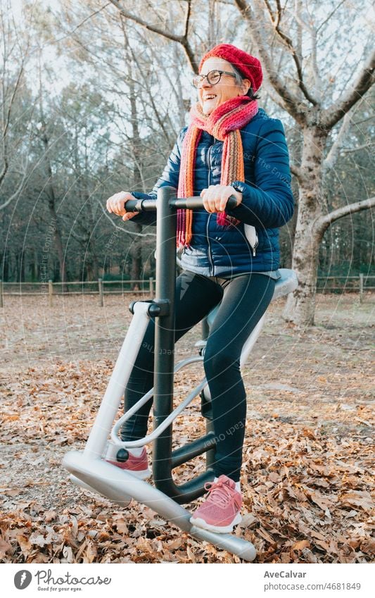 Old woman exercising on the machines in the park to keep her joints well. Happy with healthy life. Sports in nature for elderly people. Arms and legs conditioning for geriatric