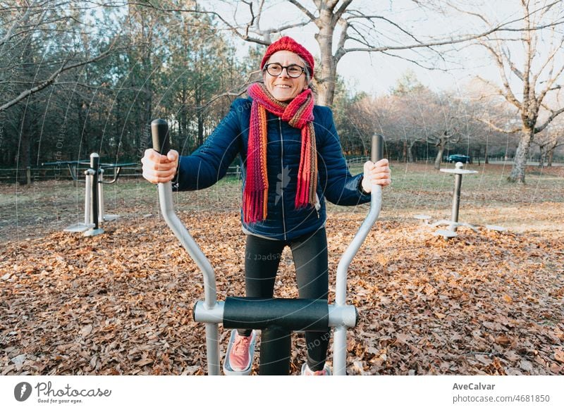 Old woman doing exercise training workout at the park on the machines to keep the articulations well. Happy with healthy life. Sport at nature senior people. Arms and legs conditioning for geriatric