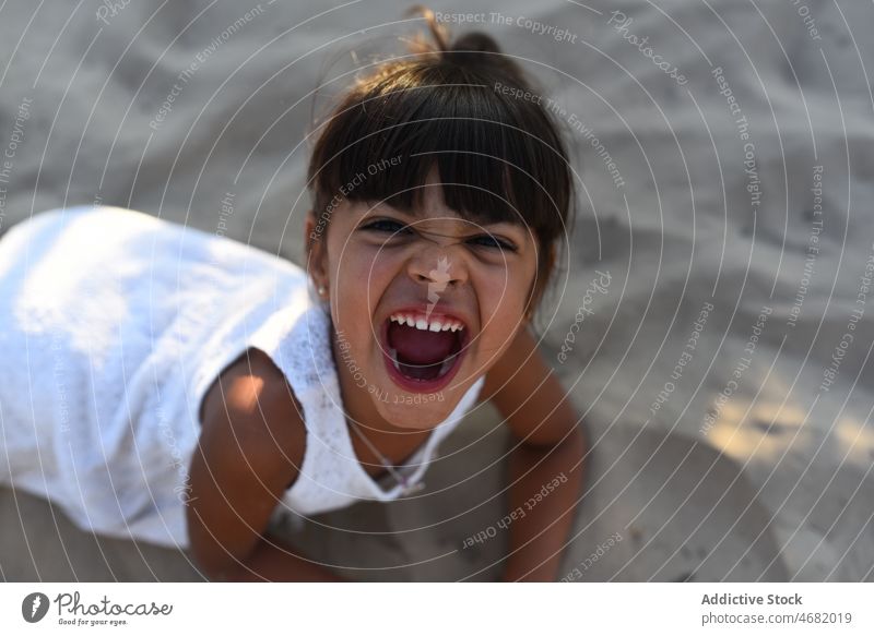 Excited girl with mouth opened on sand kid fun grimace make face beach summer playful cheerful happy excited adorable cute hispanic childhood joy friendly smile