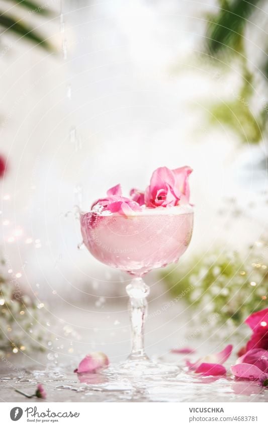 Crystal champagne glass with fancy pink drink with rose petal at white table with flowers crystal blurred branches elegant decoration front view alcohol