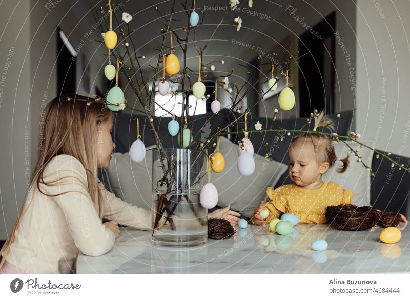 happy caucasian toddler girl eight years old and her baby sister one year old at home in living room with colored easter eggs. Stay home during Coronavirus covid-19 pandemic