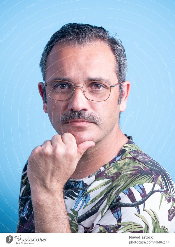 Portrait of a 45 year old caucasian man looking to the camera, with a moustache, wearing specs and casual clothes, isolated on blue background Man