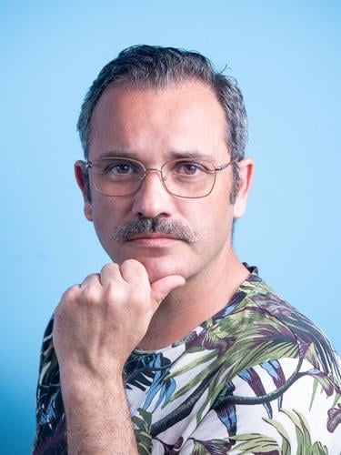 Portrait of a 45 year old caucasian man looking to the camera, with a moustache, wearing specs and casual clothes, isolated on blue background Man