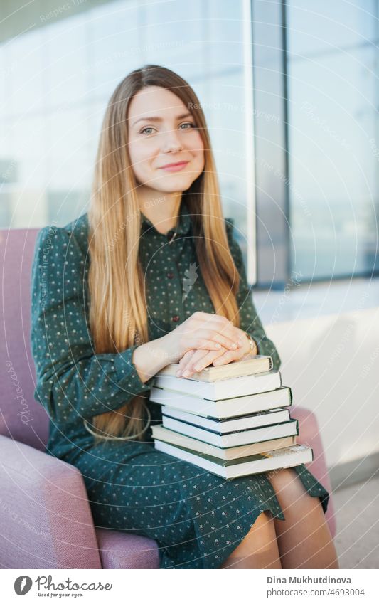 Young beautiful woman in green dress holding a stack of books. Female student holding books to study. Education and knowledge. Millennial lifestyle. University library or bookstore. Bookworm.