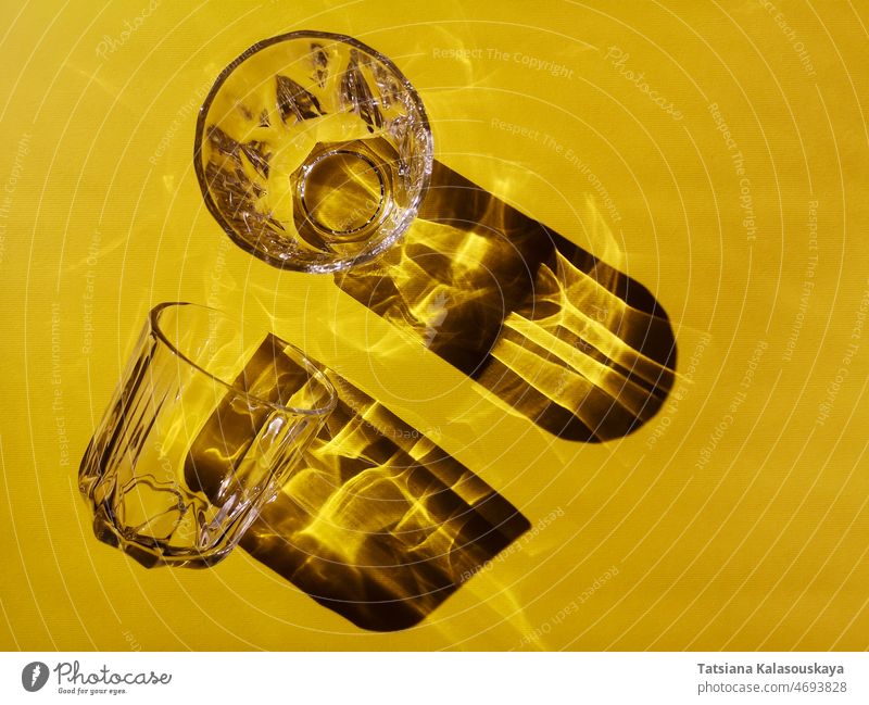 Two glass glasses on a yellow background in hard light with shadows Yellow transparent clear cup Dishes Drinks Thirst Water Cocktails Object empty cups sun beam