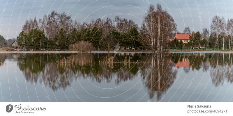 reflection of trees, houses, in spring flood water after snow melt in early spring. Overflown field and meadow in Latvia, Jelagava town, Lielupe river