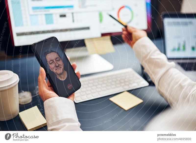 Woman entrepreneur having business video chat on smartphone with her business partner. Businesswoman working with data on charts, graphs and diagrams on computer screen