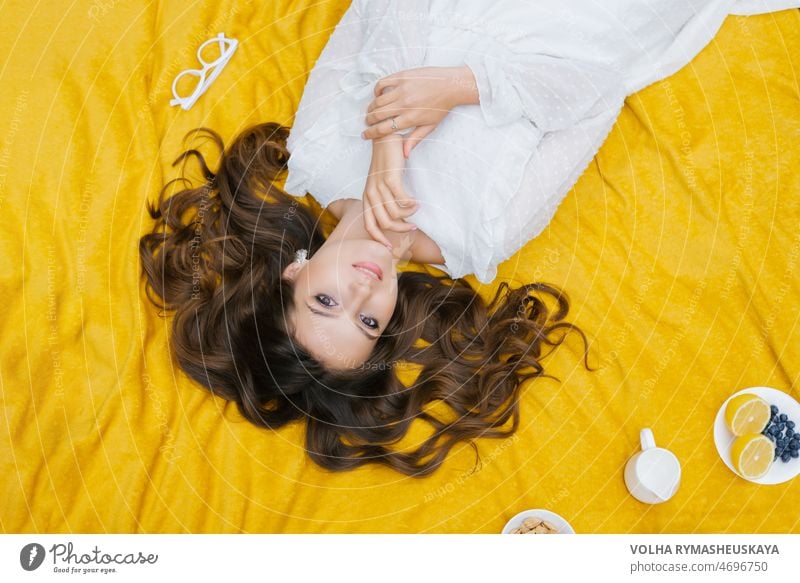 Top view of a beautiful romantic woman in a dress, lying on the green grass on a yellow blanket. Picnic in the park. Fruit on a plate. Summer holidays. person