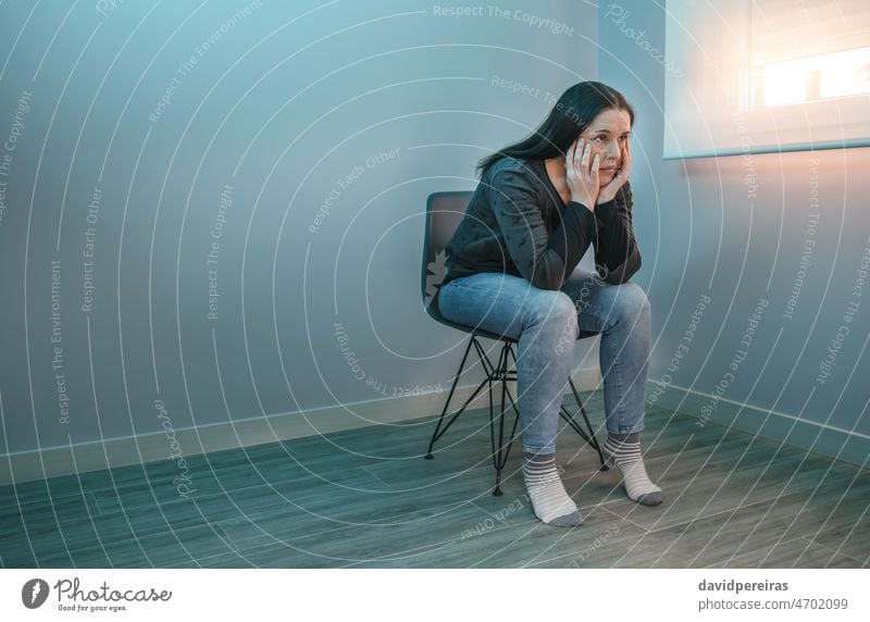 Pensive woman with lost look sitting on a chair worry pensive mental health problem uncertainty insecurity leaning hands copy space anxiety hopeless depression
