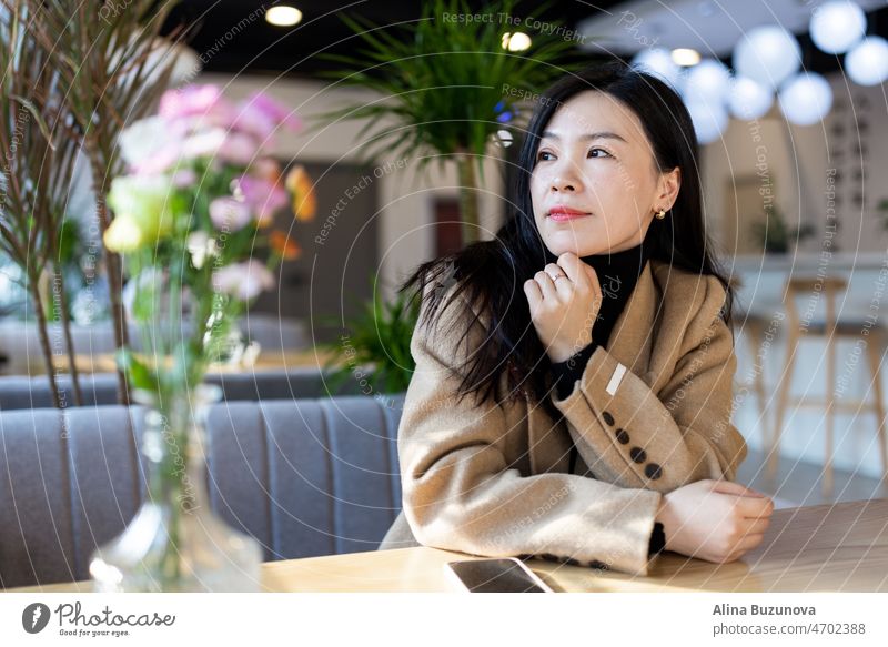 Sad tired Asian woman lonely at indoor cafe during self isolation quarantine for COVID-19 Coronavirus social distancing prevention. Mental health, anxiety depressed thinking lady.