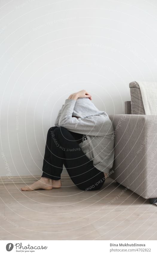 Young person in gray hoodie depressed in stress and panic attack sitting on the floor at apartment covering her head with hands in despair. Mental health issues, anxiety attack, ptsd and adhd disorder, maintaining mental health and psychology concept.
