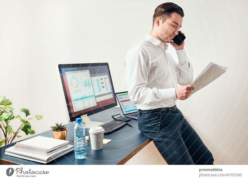 Man entrepreneur having business  conversation on mobile phone. Businessman holding documents and smartphone working with data on charts and graphs in office