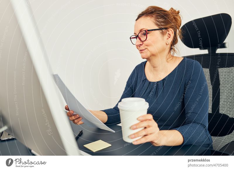 Woman entrepreneur reading financial data with satisfaction. Pleased happy business woman working in office sitting at desk using computer positive ambitious