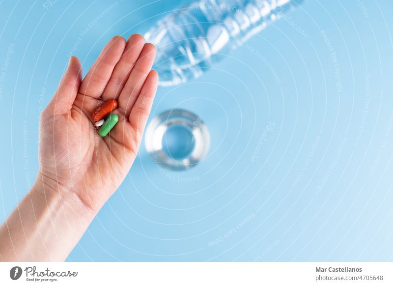 Hand showing three pills with bottle and glass of water on blue background. Health and medicine concept. hand catch health treatment body part disease healthy