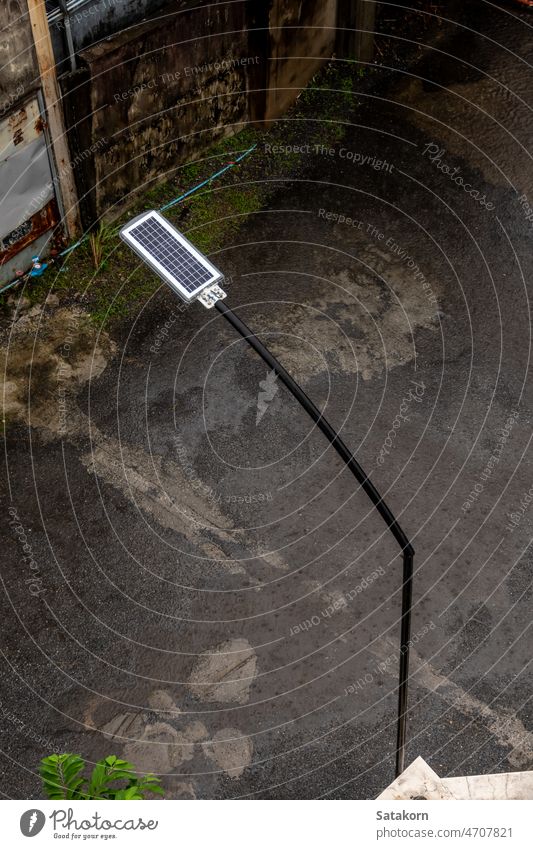 Rain falls on a small solar panel behind a street lamp in a small alley rain urban water wet weather asphalt lanterns light environment electric energy