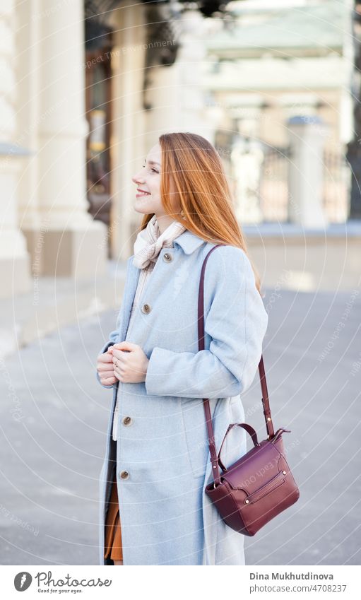 Young beautiful woman in a light blue coat standing on the street in the city in sunlight on sunny day. Candid lifestyle portrait of a woman, smiling. looking