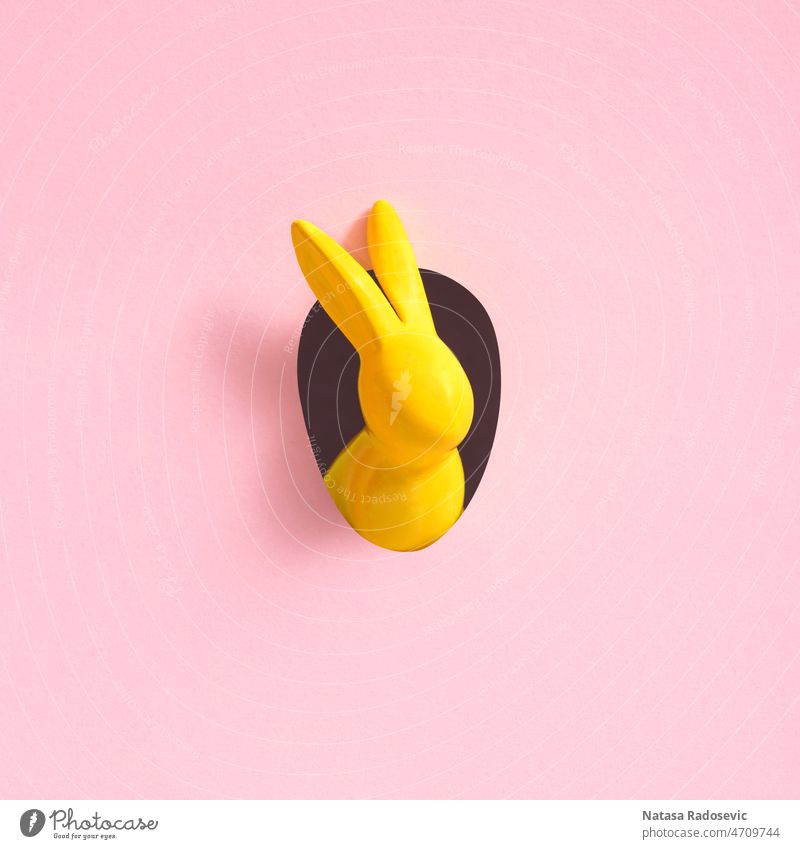 Yellow Easter bunny looks out of an egg-shaped hole in the pink background wall. easter bunny minimal copy space easter rabbit easter background no people