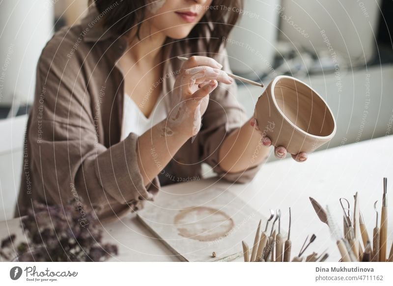 Talented woman artist creating beautiful artisanal pottery at pottery workshop, using different tool and creating a plate bowl of clay. Small female owned business.