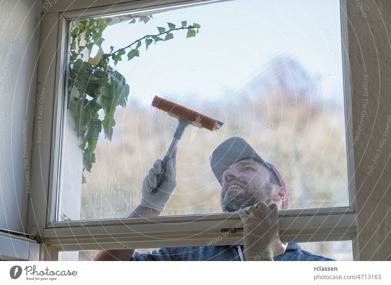 young man is using a rag and squeegee while cleaning windows. professional window cleaner care concept dirt dish soap duster equipment glass handle happy