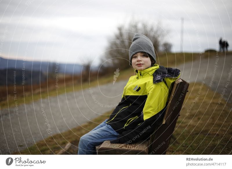 Child sitting on a bench Human being Boy (child) Infancy Exterior shot Jacket Landscape naturally Authentic Cap Weather mountains Nature windy Clouds