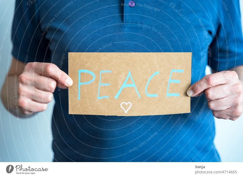 A man holds a sign with the word Peace in front of his body peace Man stop Hope Sign War Freedom Politics and state Solidarity Symbols and metaphors Humanity